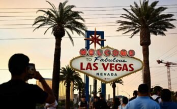Ihmiset ottavat valokuvia Fabulous Las Vegas -paneelin vastaanotolla sumuisen oranssin taivaan alla, kun aurinko laskee 29. heinäkuuta 2023.